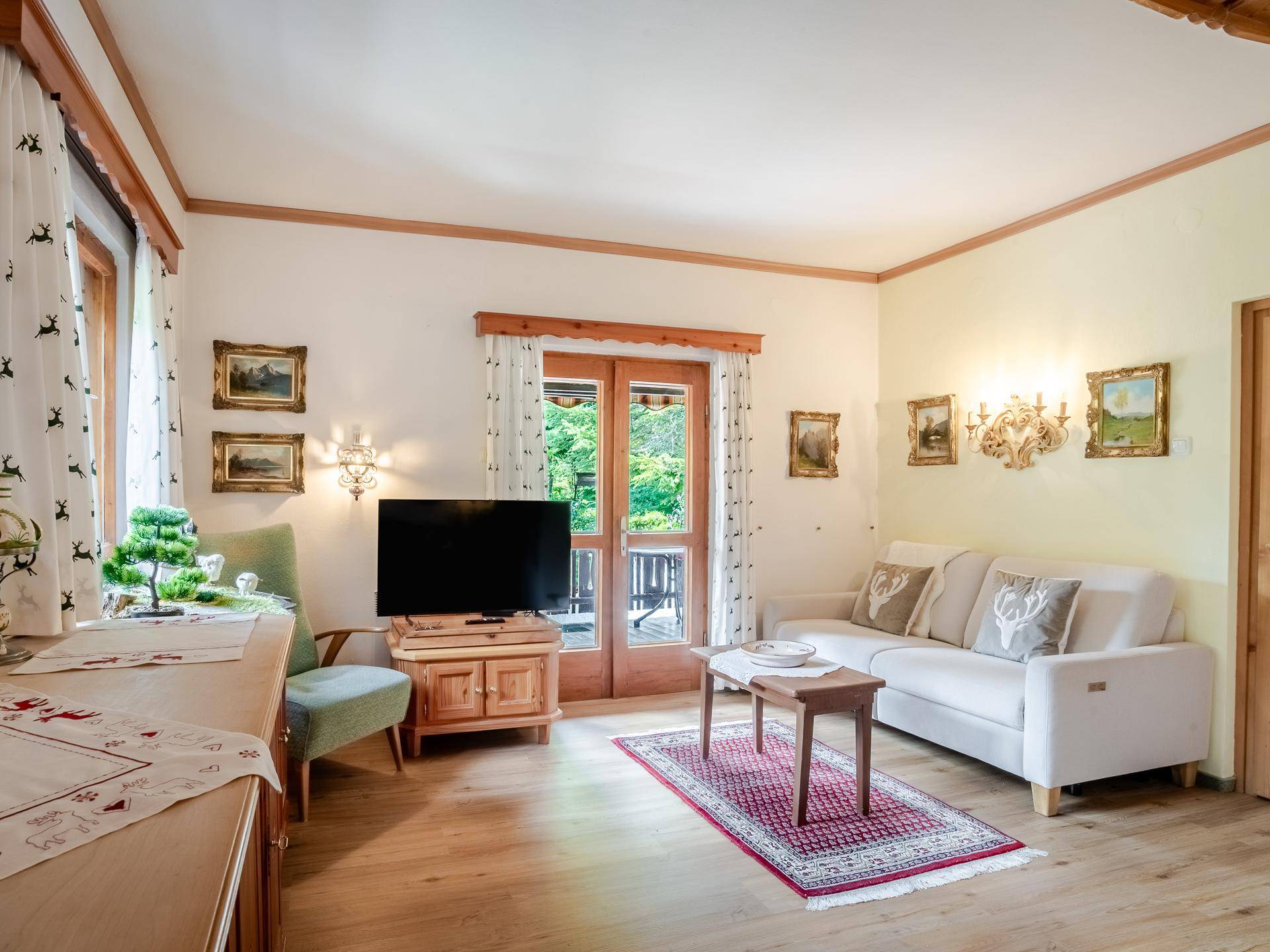 Gemütliches Wohnzimmer im alpinen Stil mit Holzboden, hellen Wänden und Balkonzugang.