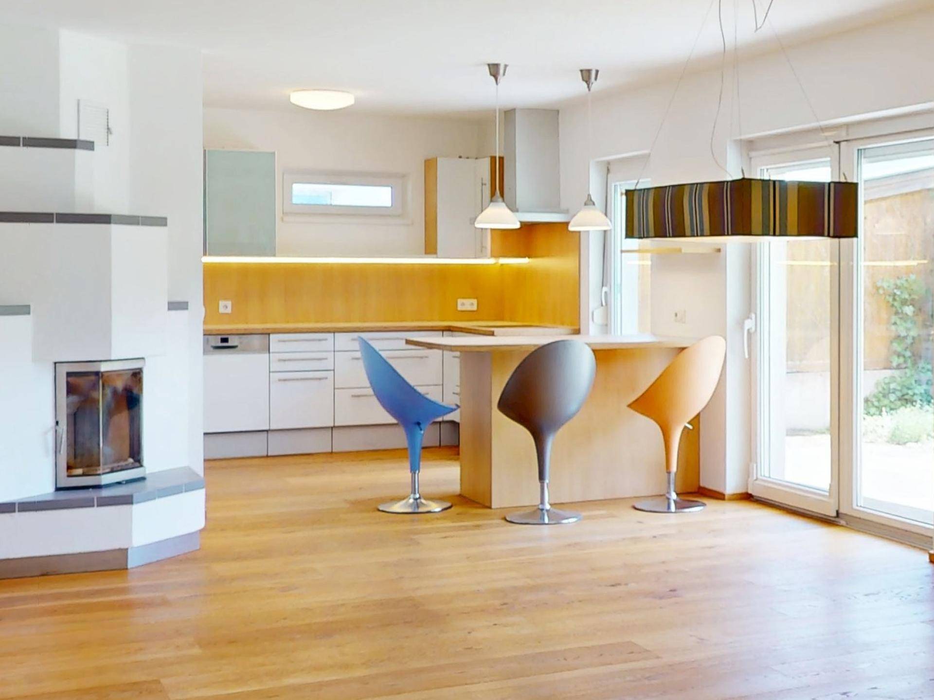Heller offener Wohn- und Essbereich mit moderner Küche, Kamin und Holzboden.