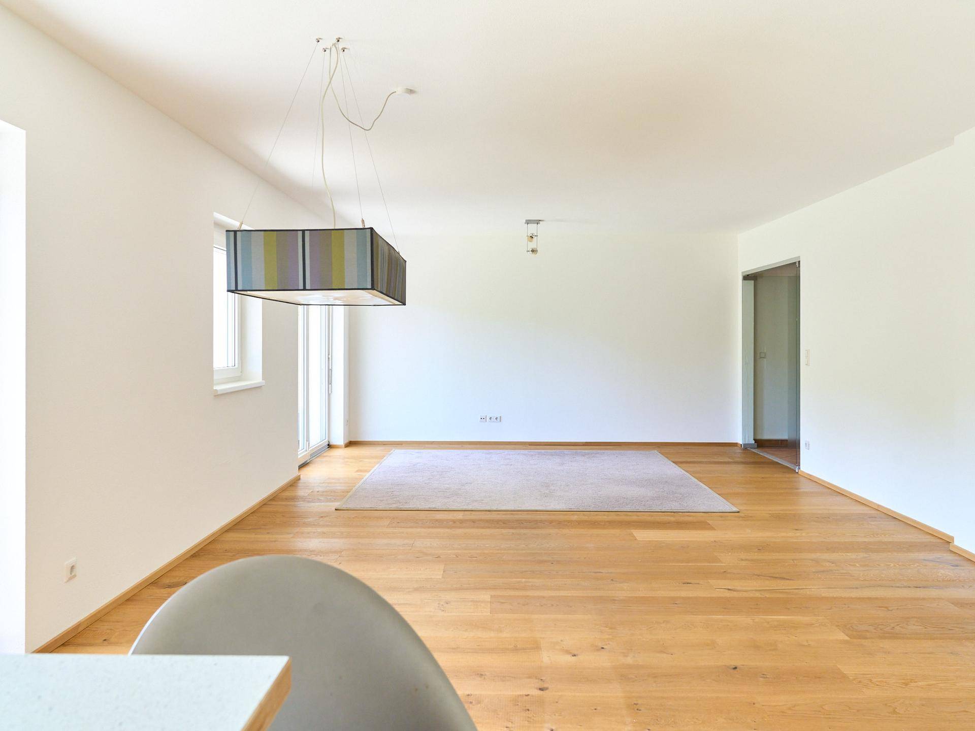 Geräumiges, leeres Wohnzimmer mit hellem Holzboden und Zugang zur Terrasse.