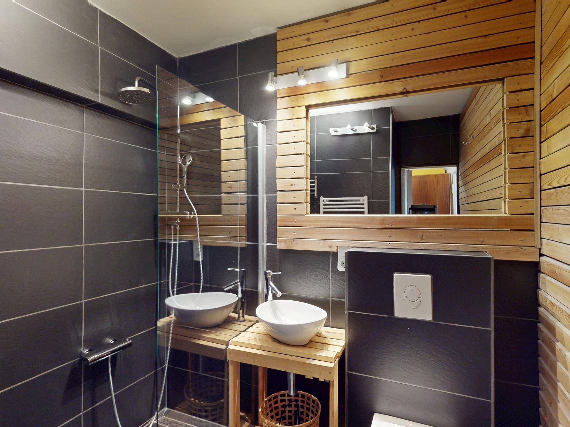 Modernes Badezimmer mit dunklen Fliesen, Holzdetails, Doppelwaschbecken und Regendusche.