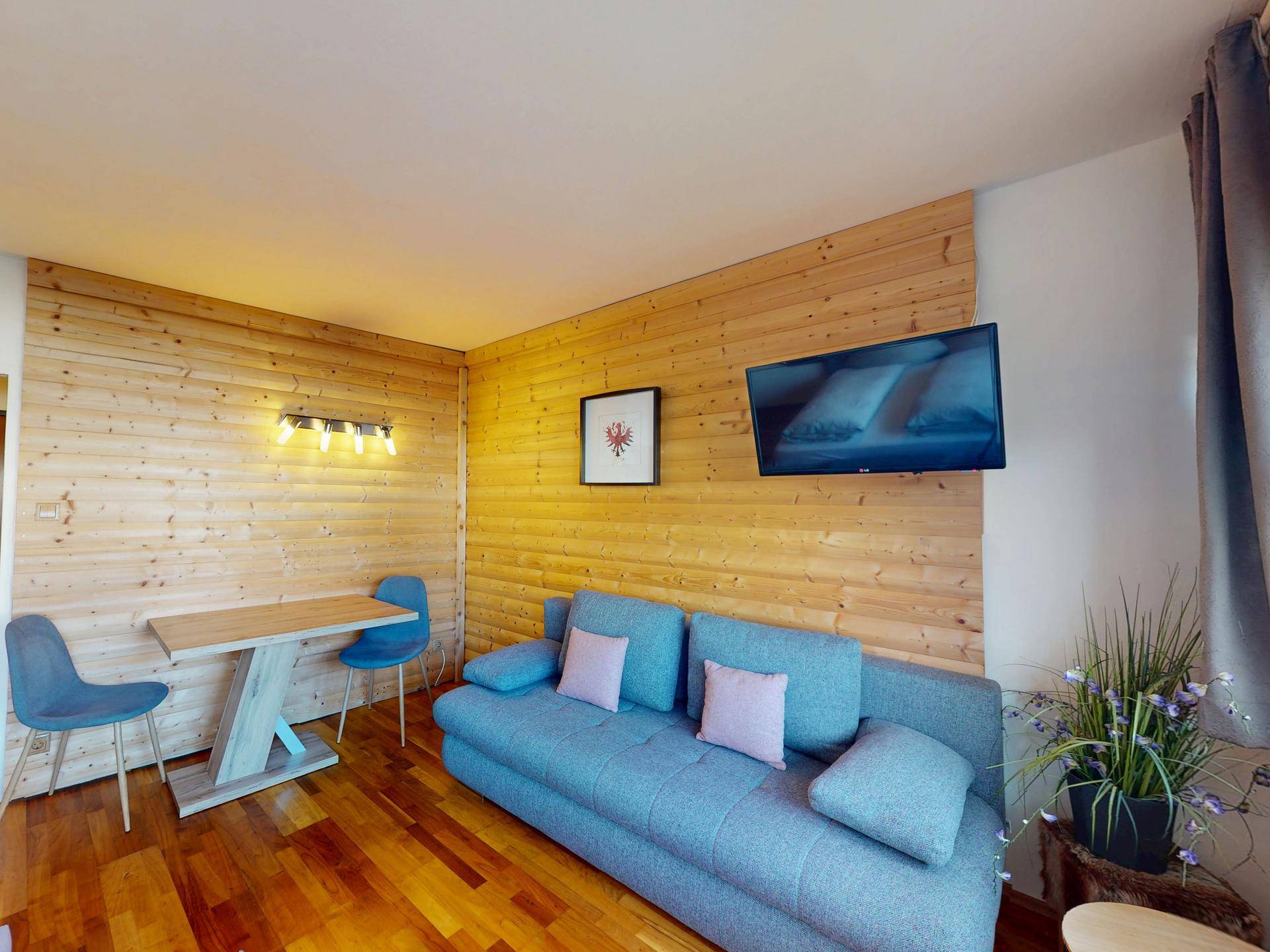 Gemütlicher Wohnbereich mit Holzwand, Sofa, Esstisch und Fernseher für entspannte Abende.