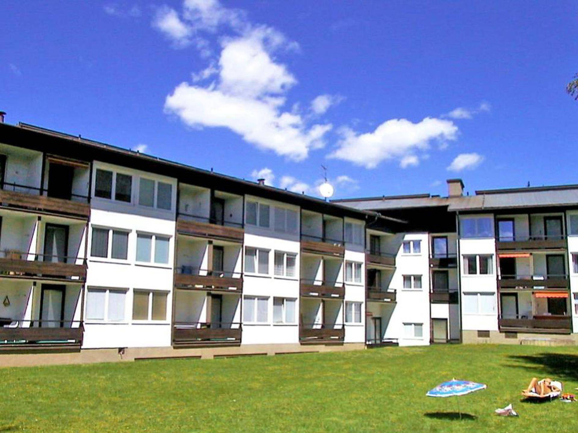 Mehrfamilienhaus mit weißer Fassade, Balkonen und einer großen Rasenfläche.
