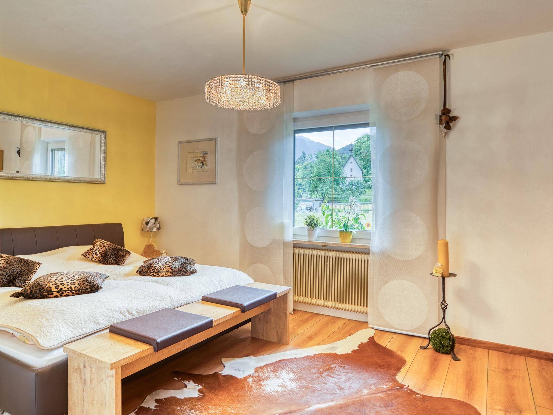 Helles Schlafzimmer mit Doppelbett, Holzboden und Blick ins Grüne durch das Fenster.