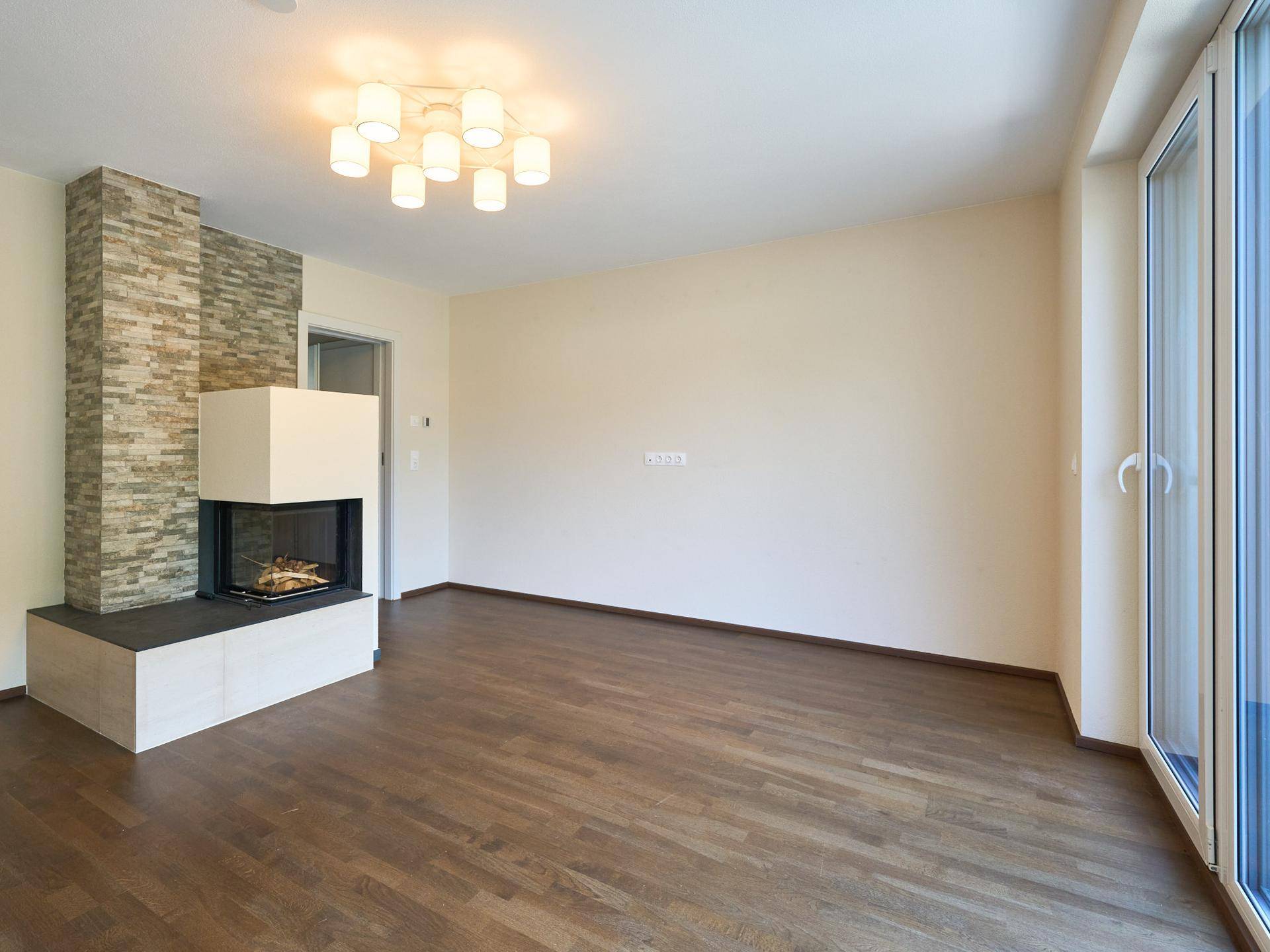Geräumiges Wohnzimmer mit modernem Kamin, dunklem Holzboden und großen Fenstern.