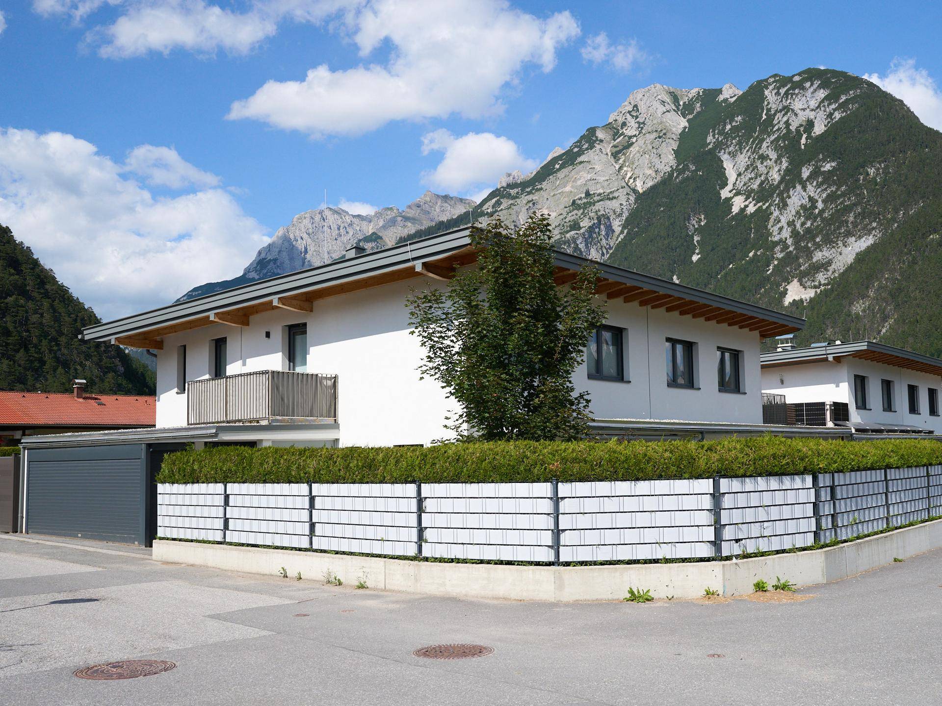 Modernes Einfamilienhaus mit Garage, Zaun und Bergblick in sonniger Umgebung.