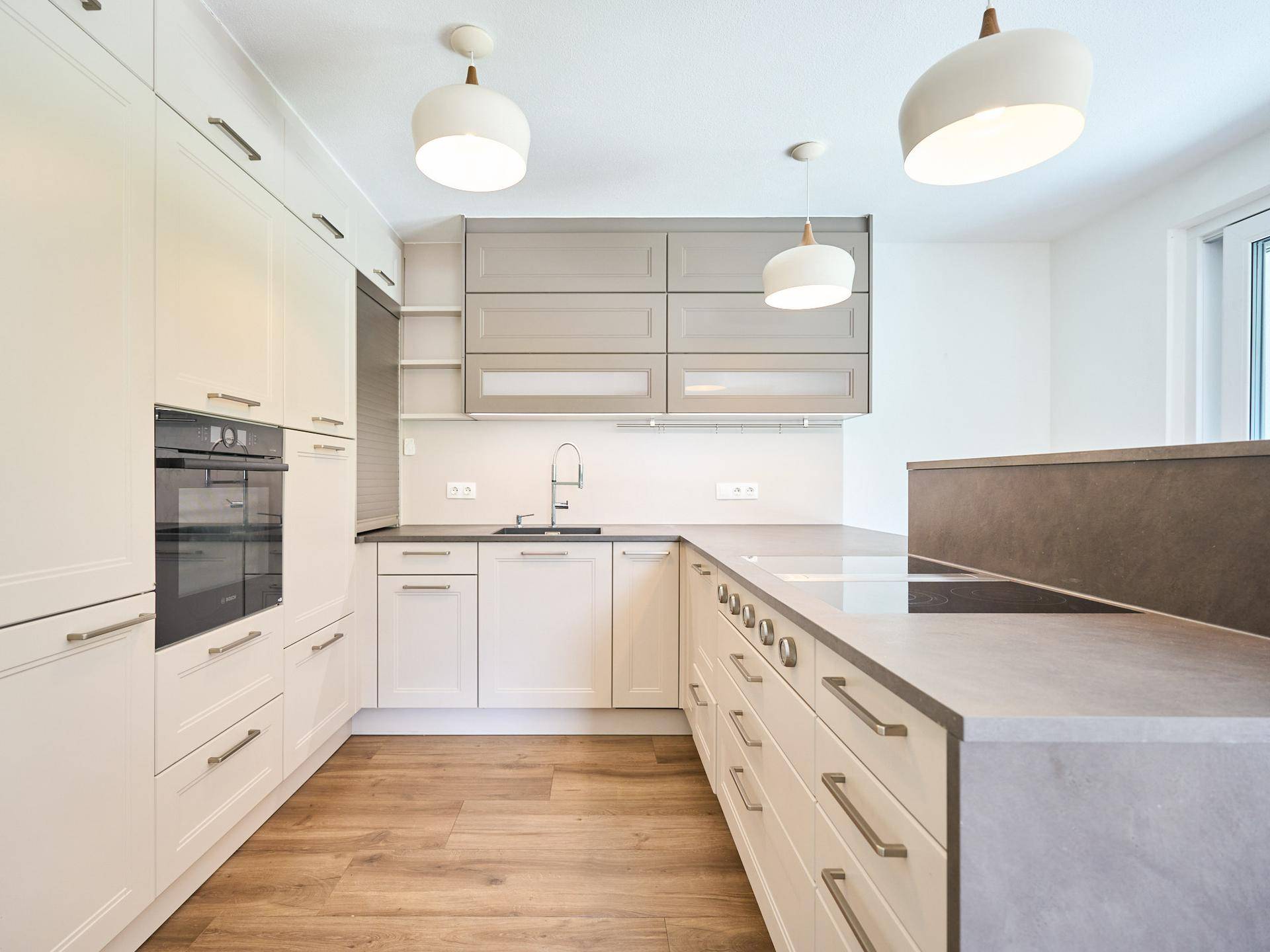 Helle, moderne Küche mit beigen Schränken, Holzboden und integrierten Geräten.