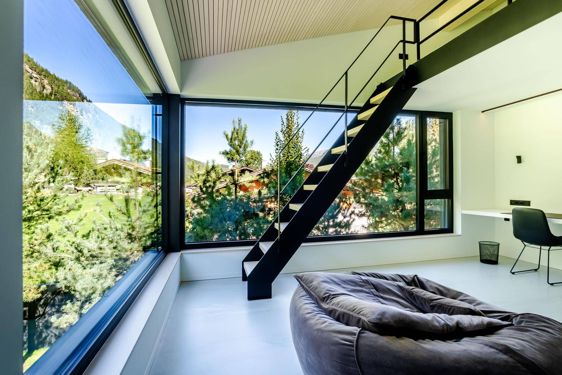 Schlafzimmer mit Loft-Charakter, offener Treppe und raumhohen Fenstern mit Bergblick.