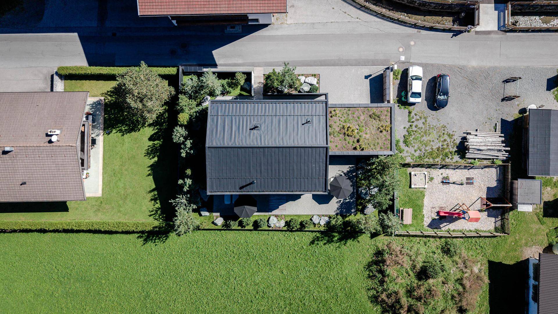 Luftaufnahme des modernen Hauses mit Flachdach, Garten und angrenzender Straße.