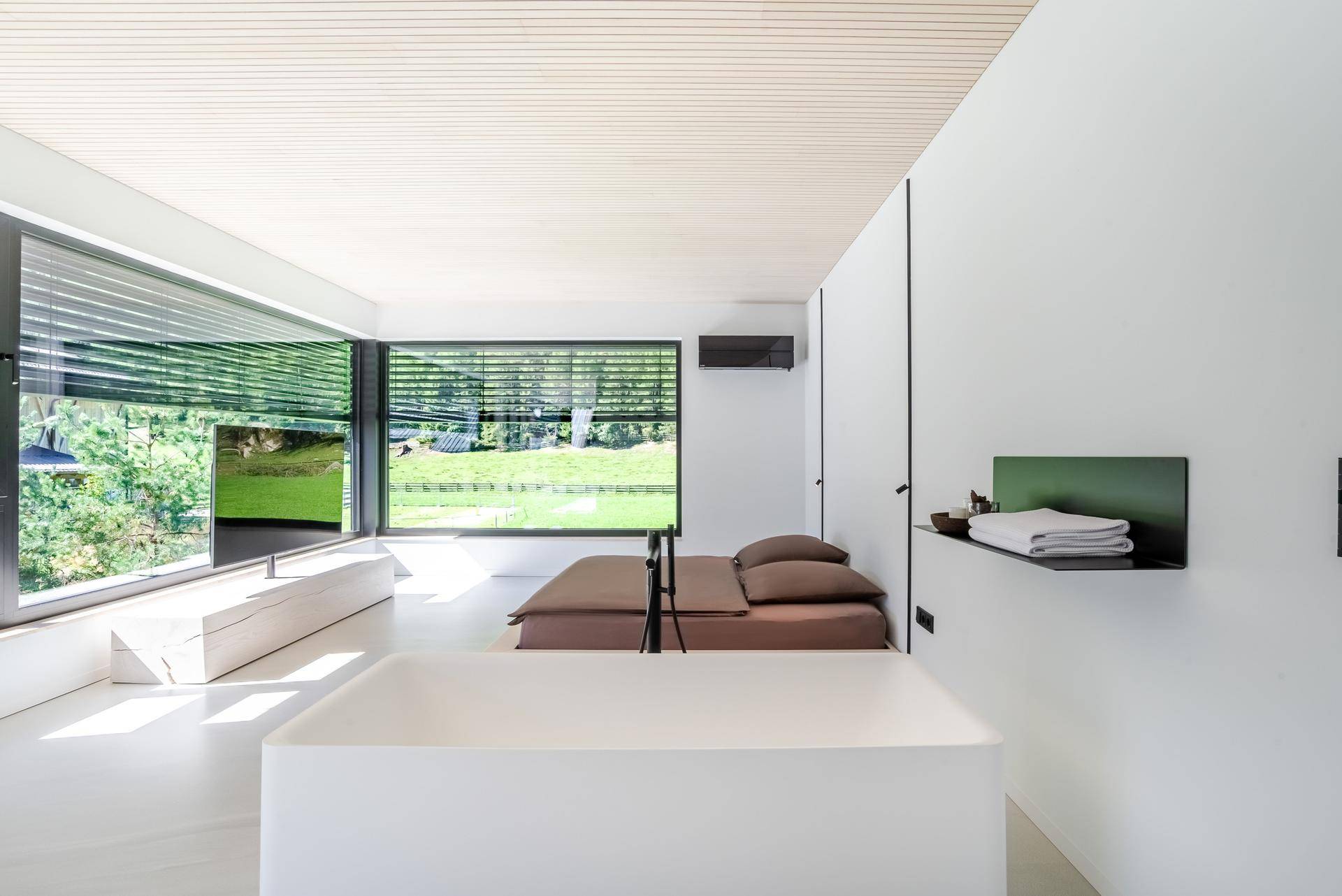 Modernes Schlafzimmer mit freistehender Badewanne und großen Fenstern mit Blick ins Grüne.