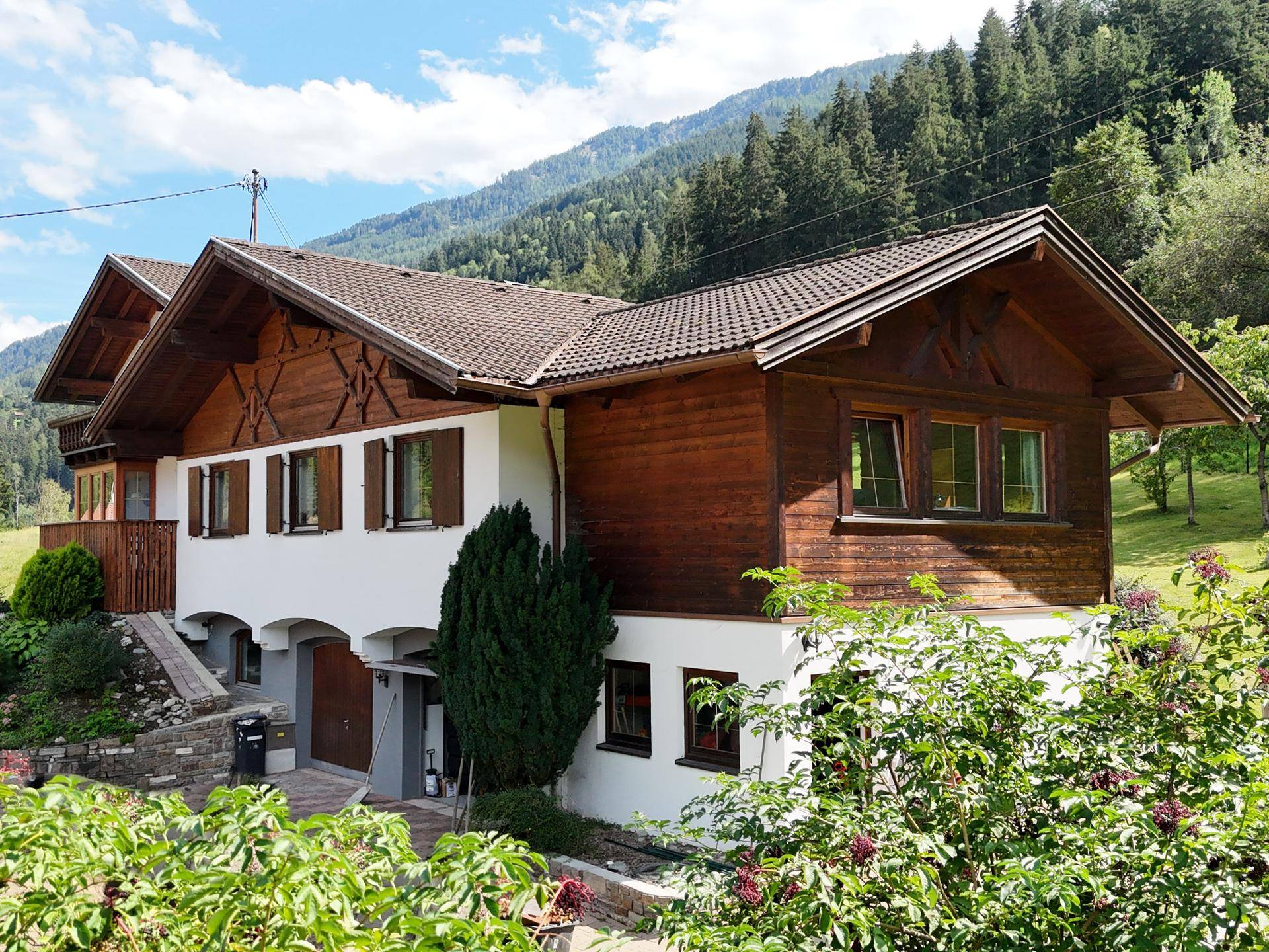 Charmantes Landhaus mit Holzelementen und Satteldach, eingebettet in eine grüne Berglandschaft.