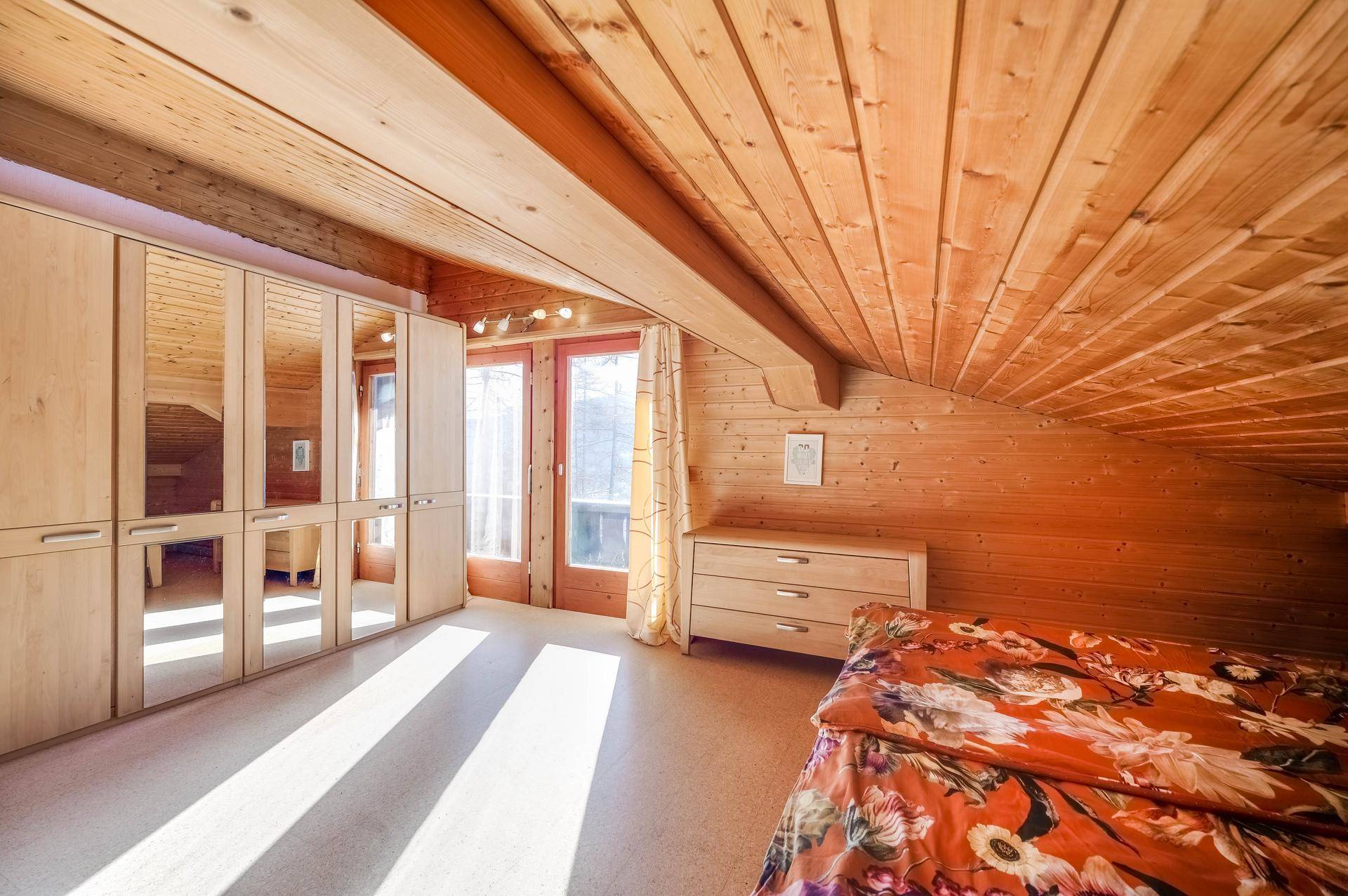 Helles Schlafzimmer im Dachgeschoss mit Holzverkleidung, Dachschräge und Spiegelschränken.