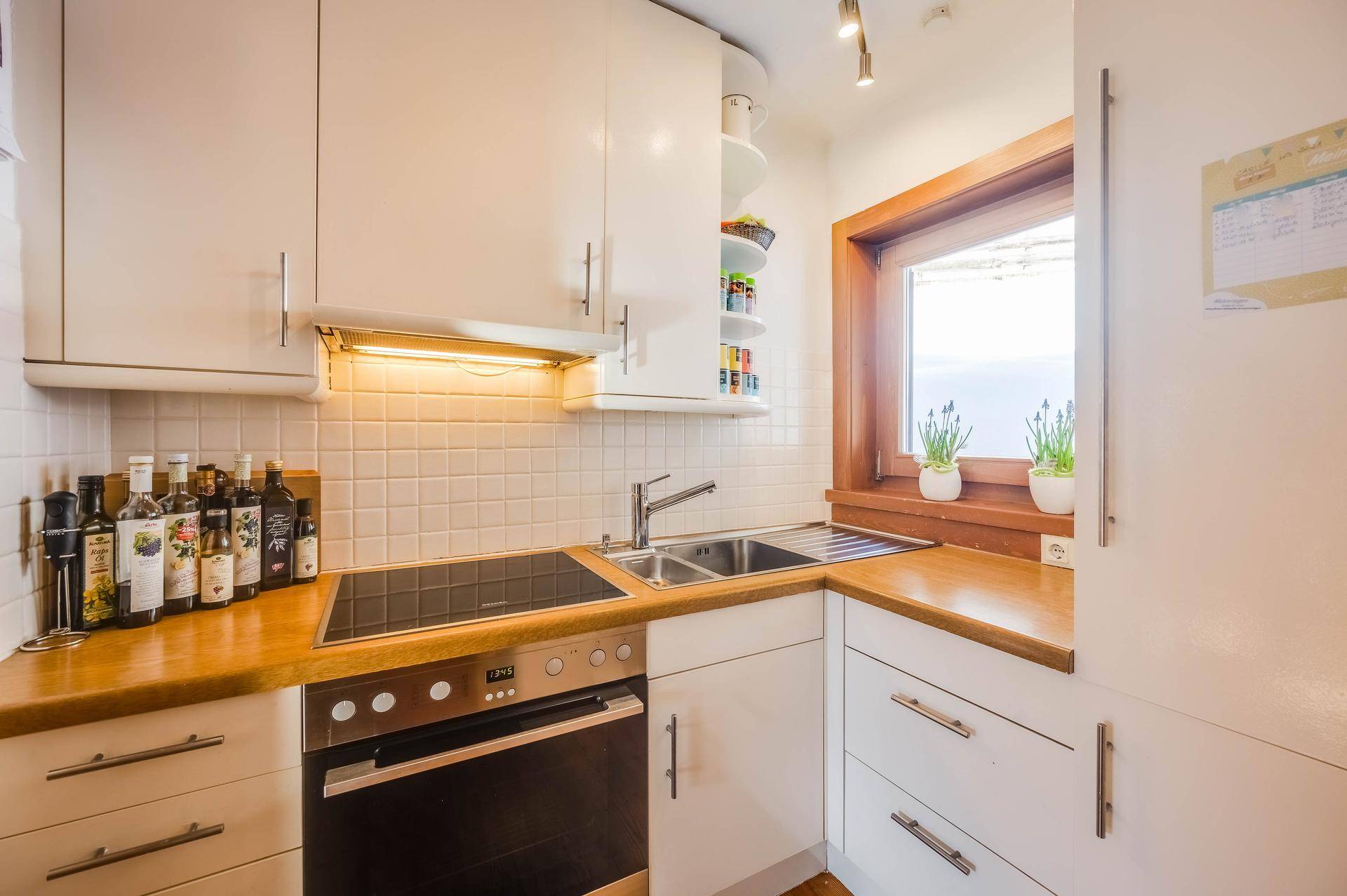 Kleine, funktionale Küche mit weißen Schränken, Holz-Arbeitsplatte und Fenster.