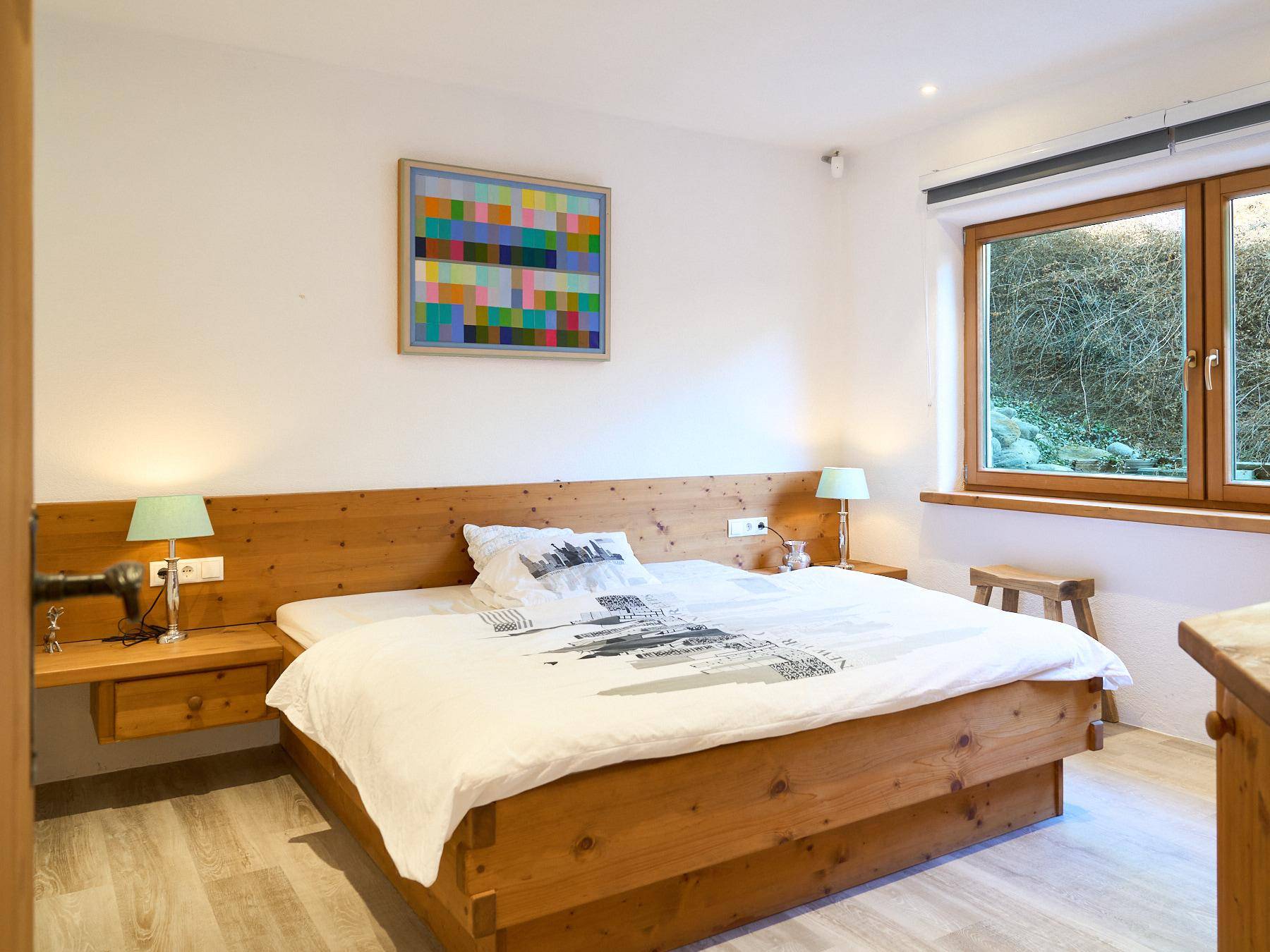 Komfortables Schlafzimmer mit Holzbett, Nachttischen und farbenfrohem Kunstwerk.