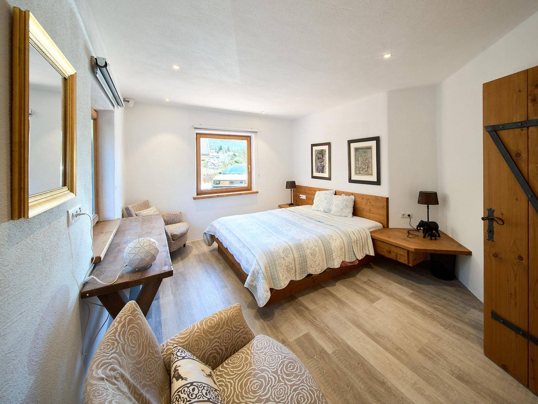 Helles Schlafzimmer mit Holzbett, Sitzgelegenheiten und Blick ins Grüne.