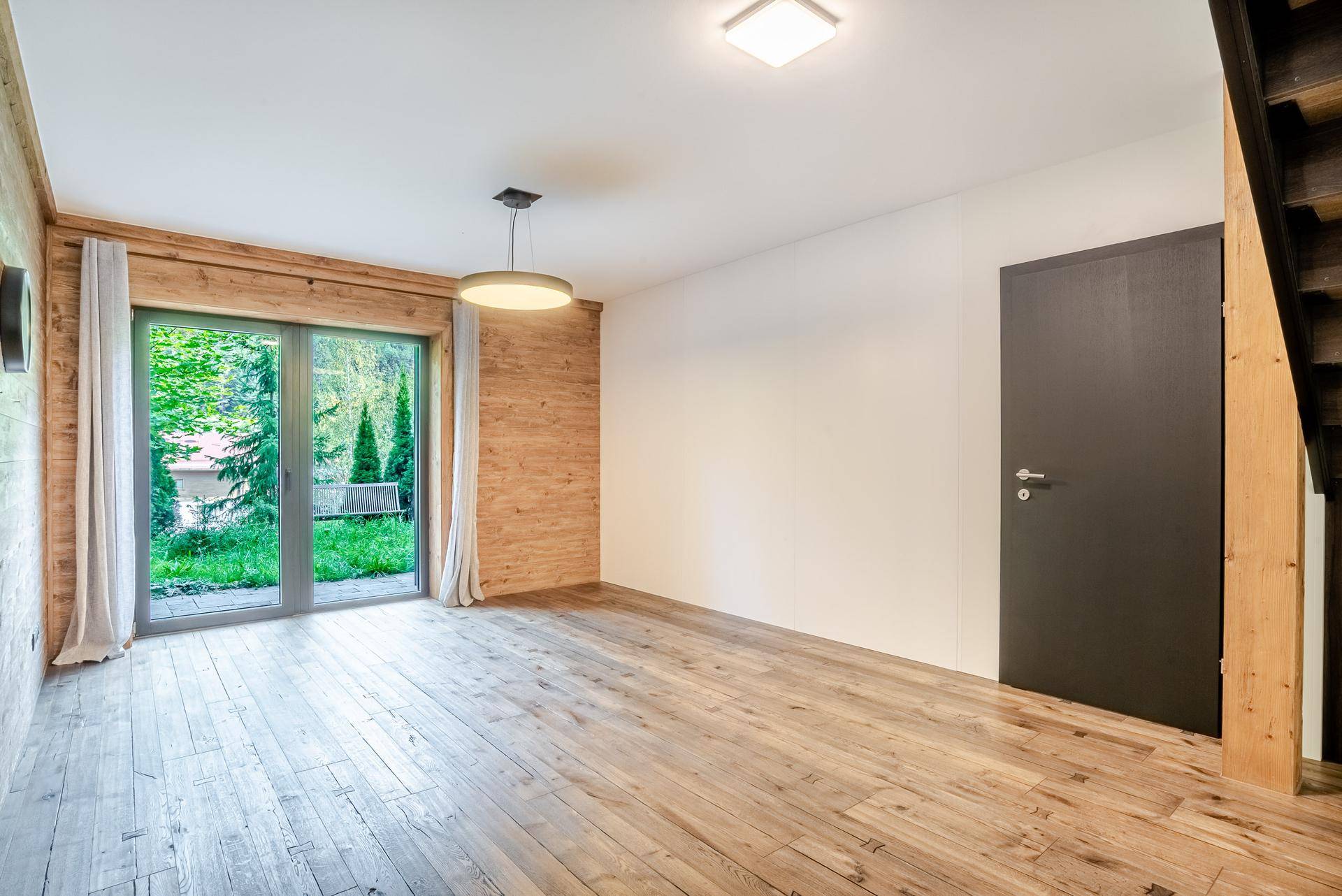 Leerer Raum mit Holzwänden, Parkettboden und Zugang zu einem kleinen Gartenbereich.