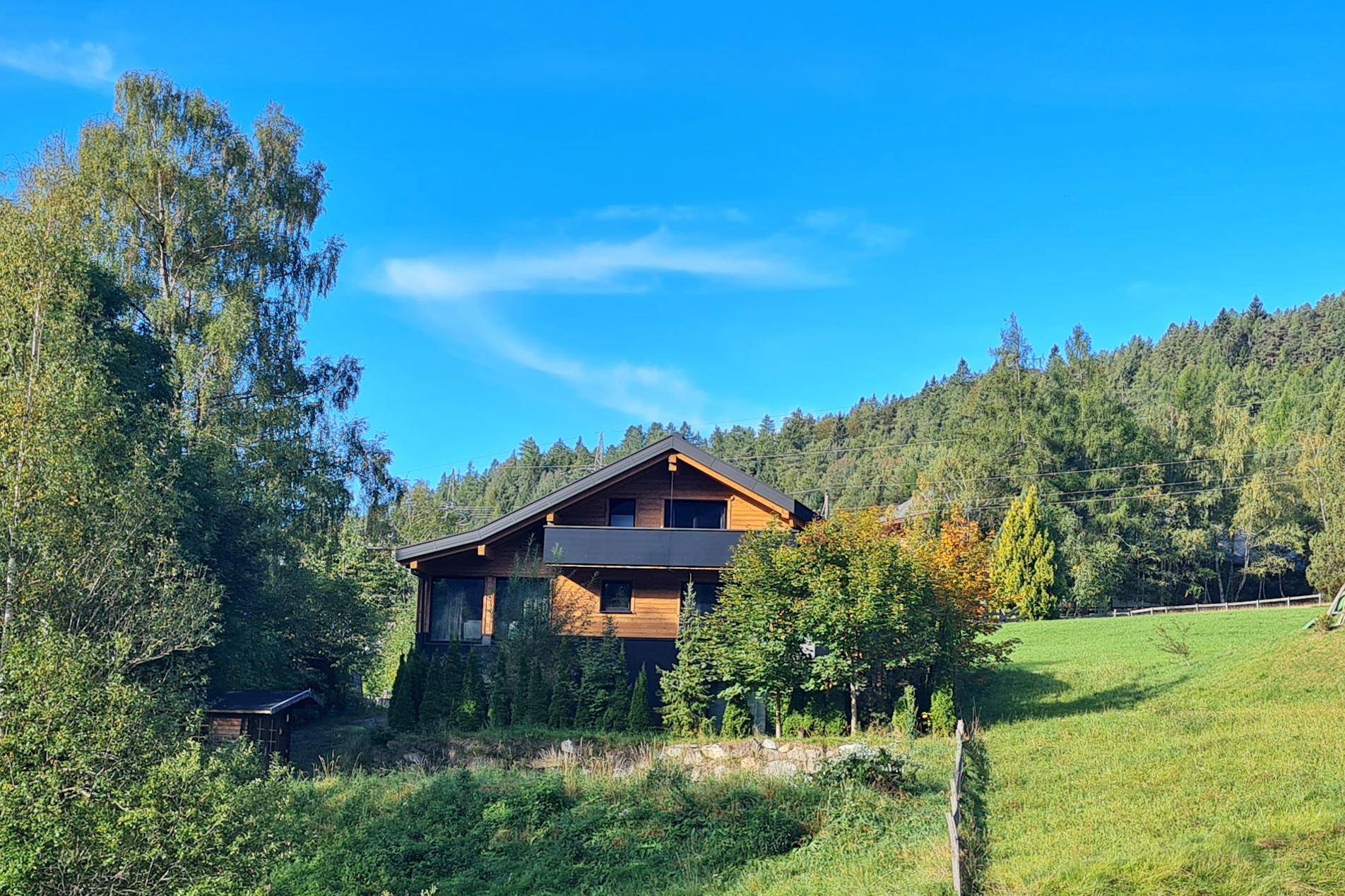 Charmantes Holzhaus eingebettet in eine grüne Landschaft mit Wald und Wiesen.