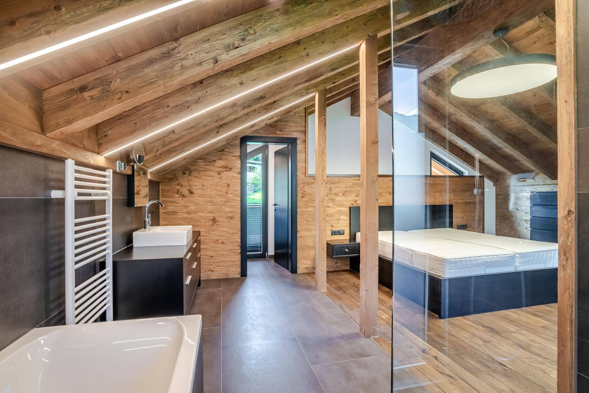 Modernes Badezimmer im Dachgeschoss mit Badewanne, Einzelwaschbecken und Holzwänden.