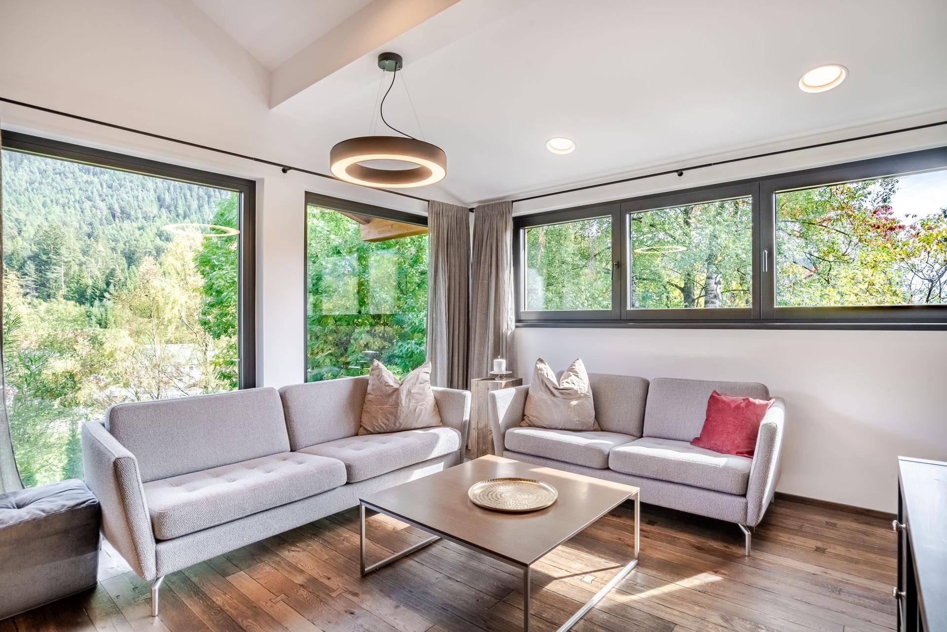 Helles Wohnzimmer mit modernen Sofas, Holzboden und großen Fenstern mit Blick ins Grüne.