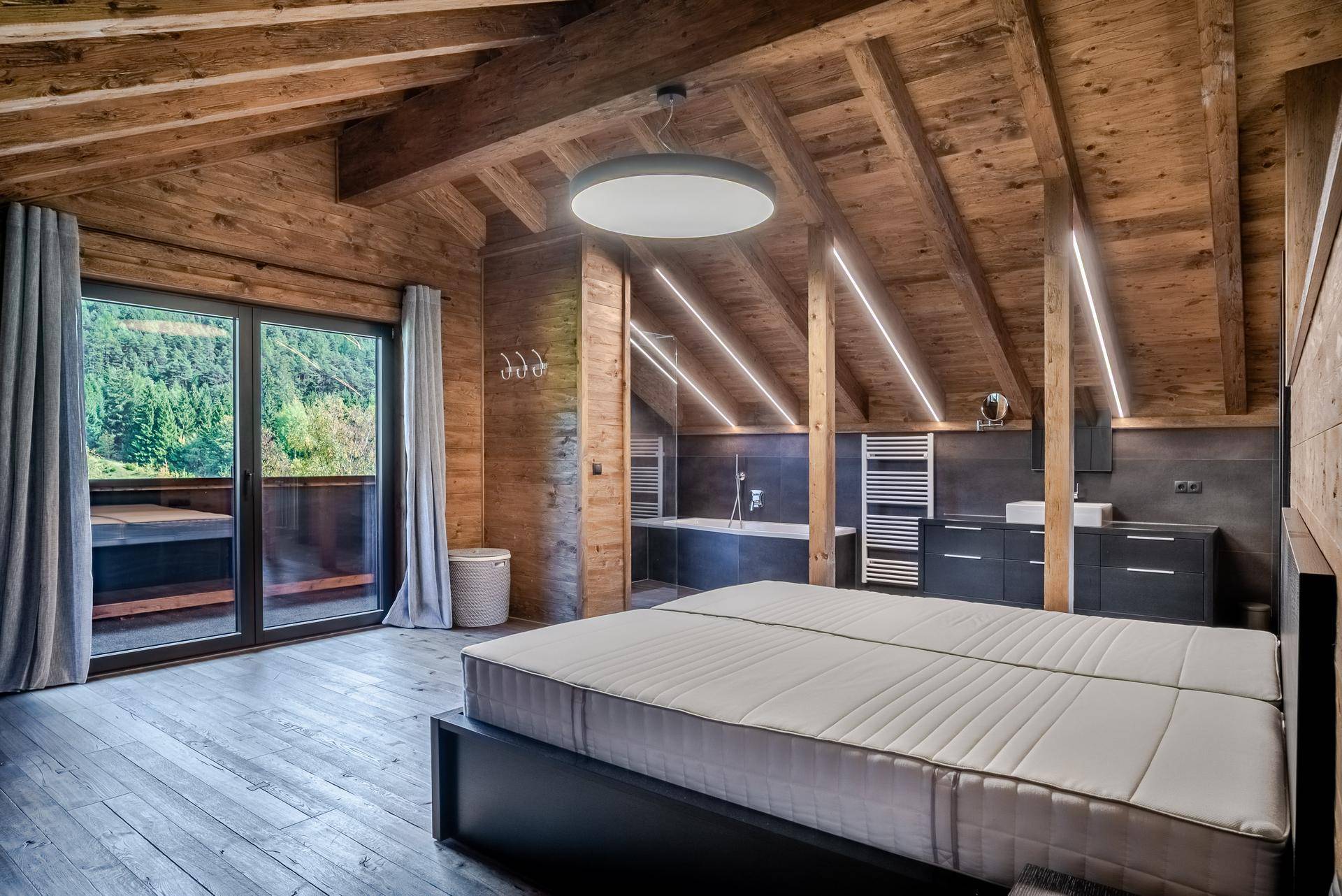 Schlafzimmer im Dachgeschoss mit Holzbalken, integriertem Badbereich und Zugang zum Balkon.