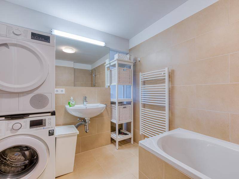Modernes Badezimmer mit Badewanne, Waschbecken und Waschmaschine mit Trockner.