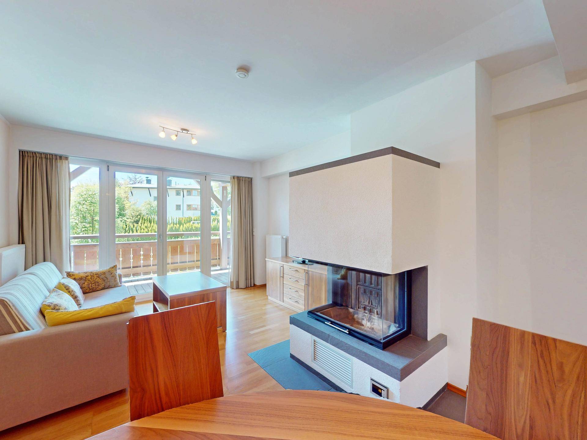 Helles Wohnzimmer mit Kamin, Holzboden und großen Fenstern zum Balkon.