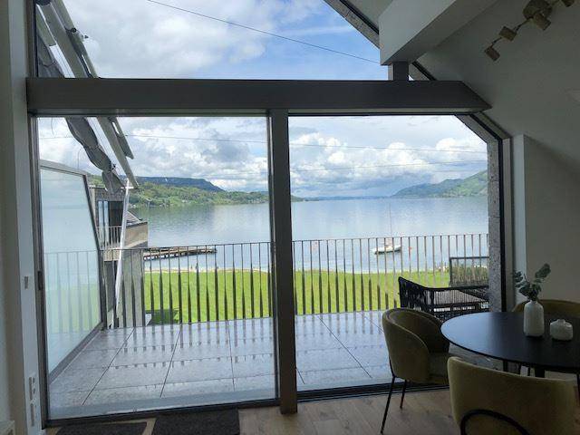 Heller Wohnbereich mit Zugang zur Terrasse und weitem Blick auf den See und die Berge.