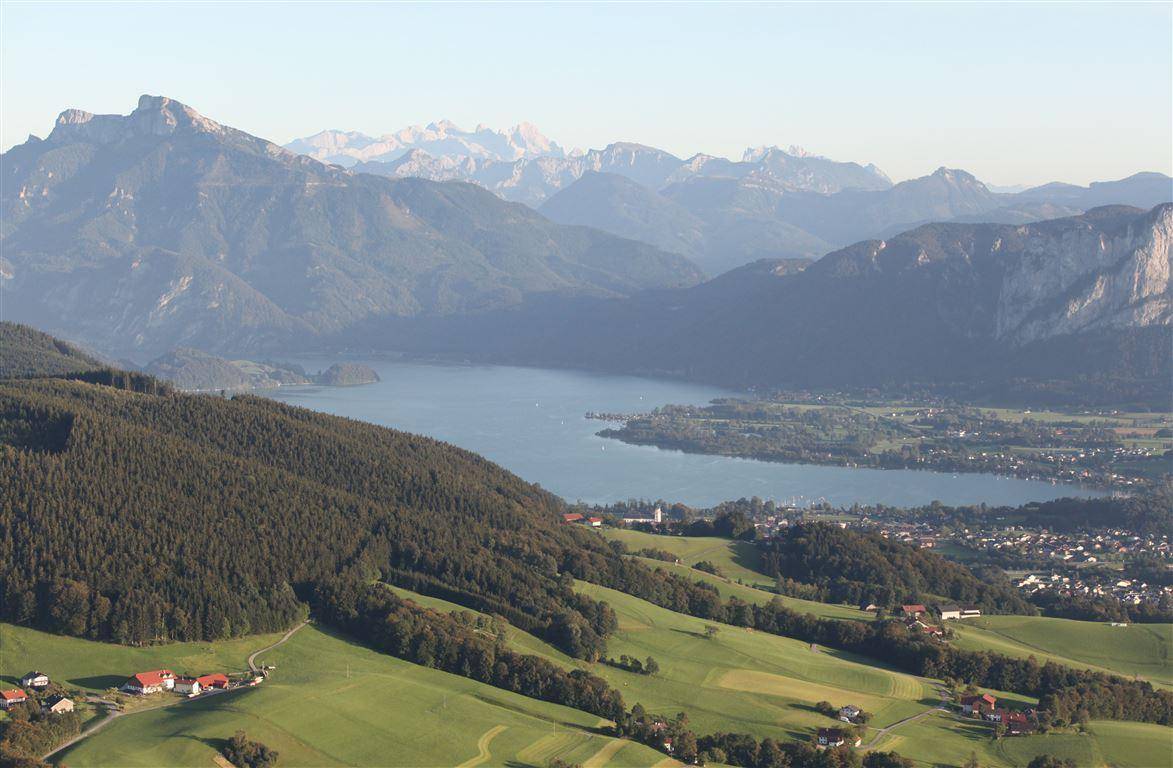 Weitläufiger Ausblick über eine Seenlandschaft mit bewaldeten Hängen und fernen Berggipfeln.