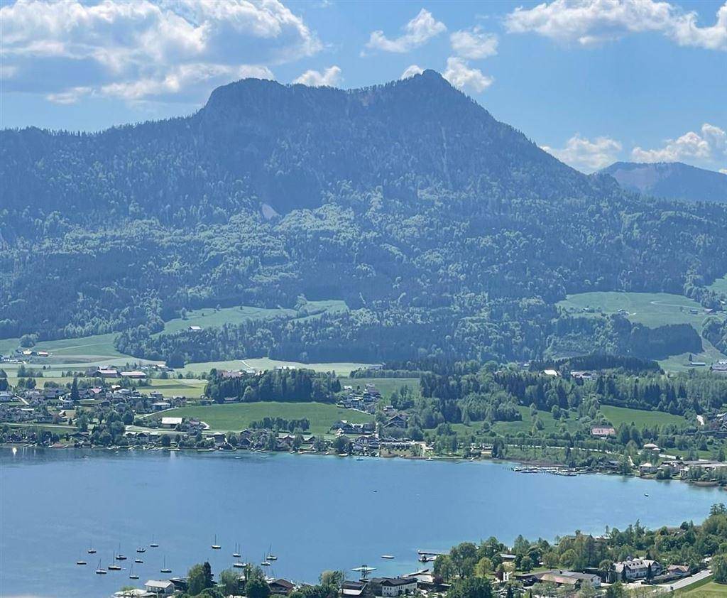 Panoramablick auf einen malerischen See, umgeben von grünen Hügeln und Bergen.