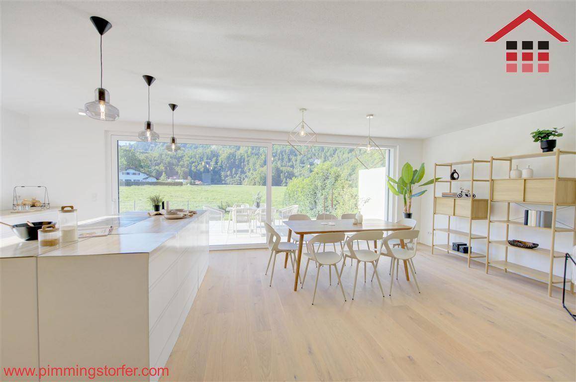 Heller, offener Wohn-Essbereich mit moderner Küche, Holzboden und großen Fenstern mit Bergblick.