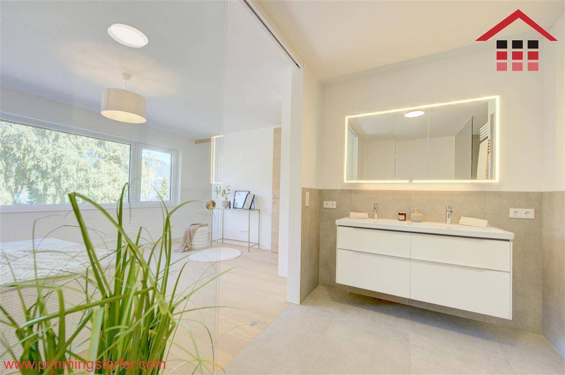 Modernes Badezimmer mit Doppelwaschbecken, beleuchtetem Spiegel und Blick ins angrenzende Schlafzimmer.