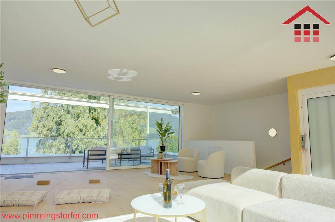 Lichtdurchflutetes Wohnzimmer mit großen Fensterfronten, Holzboden und Zugang zur Terrasse mit Seeblick.