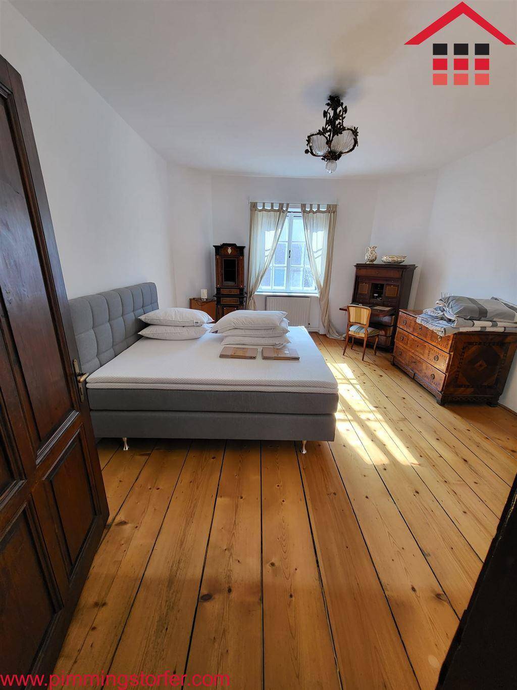 Geräumiges Schlafzimmer mit Holzdielenboden, großem Bett und antiken Möbeln, lichtdurchflutet.