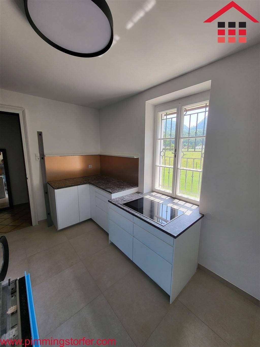 Helle Küche mit weißen Unterschränken, Induktionskochfeld und Fenster mit Blick ins Grüne.