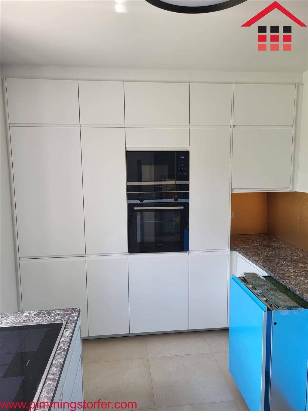 Moderne Einbauküche mit weißen Schränken, integriertem Backofen und Mikrowelle für effizientes Kochen.