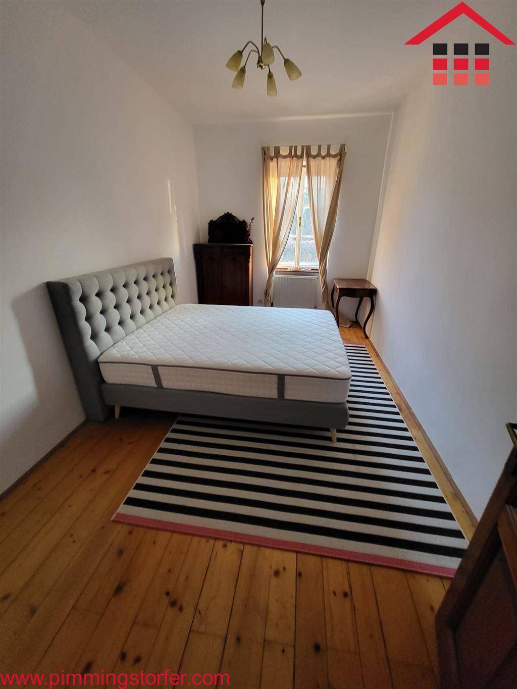 Helles Schlafzimmer mit Holzdielenboden, modernem Bett und einem Fenster mit Vorhängen.