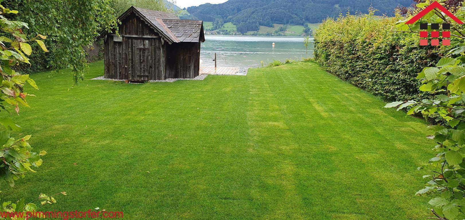 Gepflegter Rasenbereich mit einem kleinen Holzschuppen direkt am Seeufer und einer Hecke.