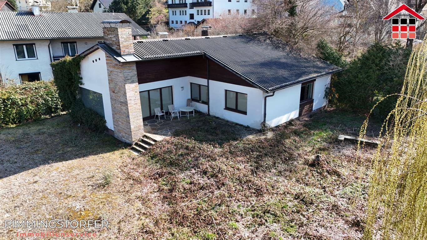 Rückansicht des Hauses mit kleiner Terrasse, Gartenmöbeln und einem weitläufigen, ungestalteten Garten.