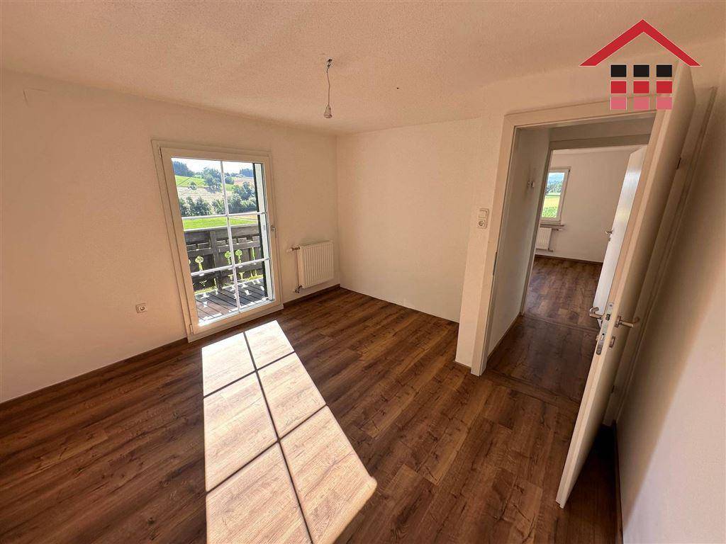 Schlafzimmer mit Laminatboden, Zugang zum Balkon und Blick auf die grüne Landschaft.
