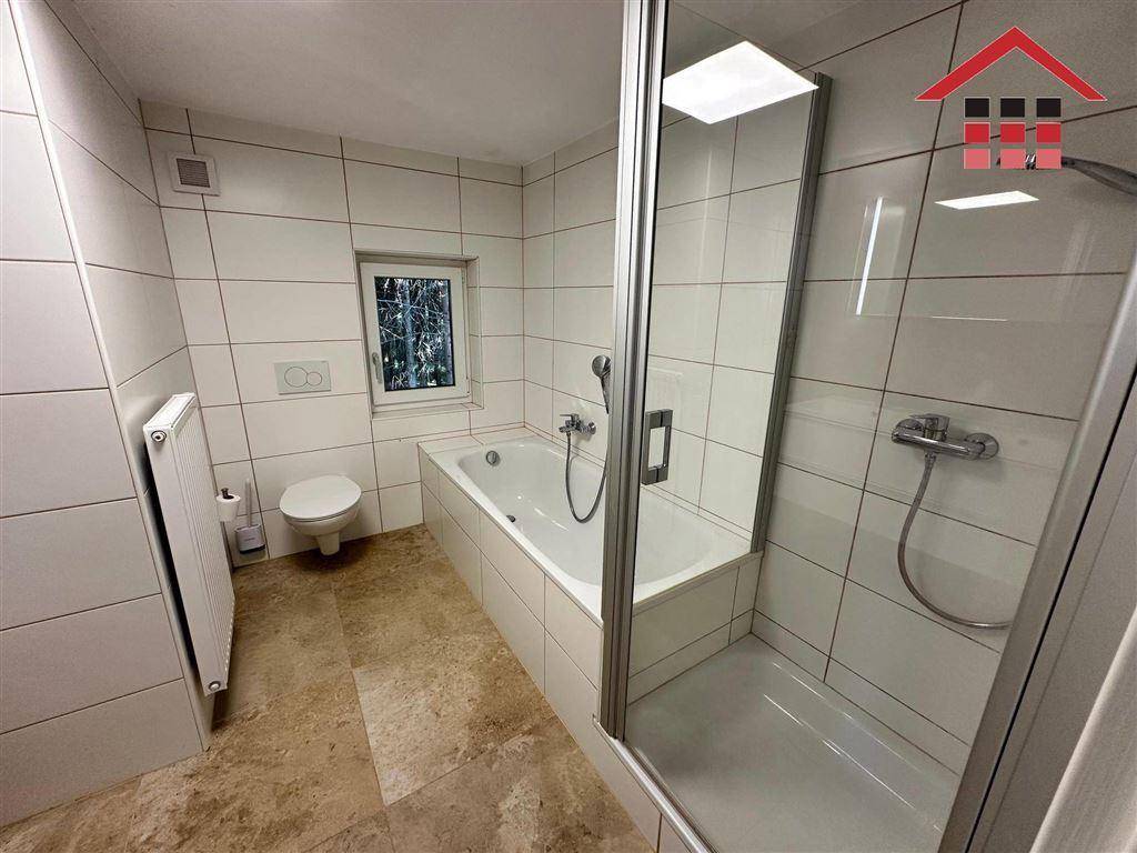 Modernes Badezimmer mit Badewanne, separater Dusche und Wand-WC in hellen Fliesen.