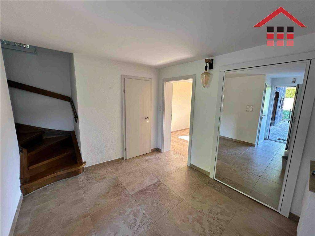 Heller Flur mit Fliesenboden, Holztreppe und großem Spiegel, der den Raum erweitert.