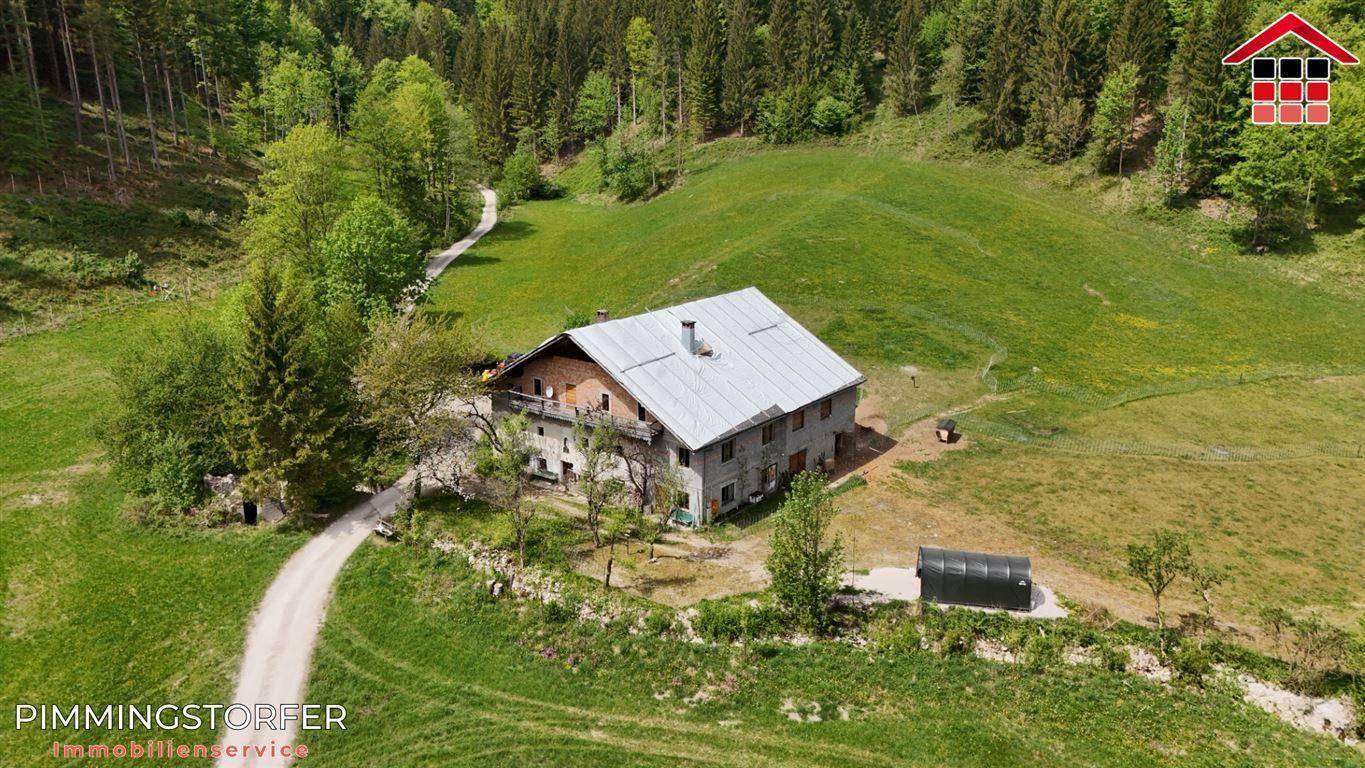 Luftaufnahme eines traditionellen Landhauses mit Satteldach, umgeben von grünen Hügeln und Bäumen.