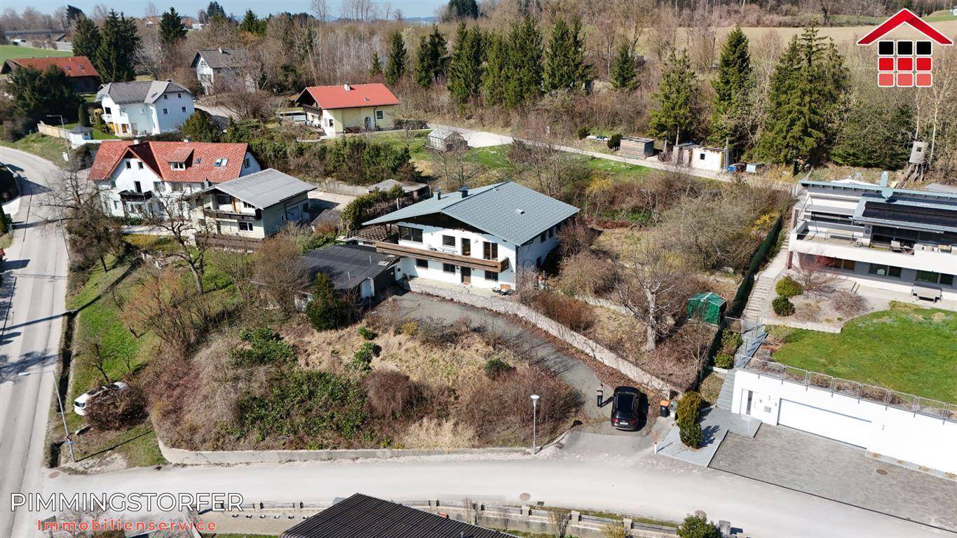 Drohnenaufnahme eines Einfamilienhauses mit Zufahrt und Nachbargebäuden in grüner Umgebung.