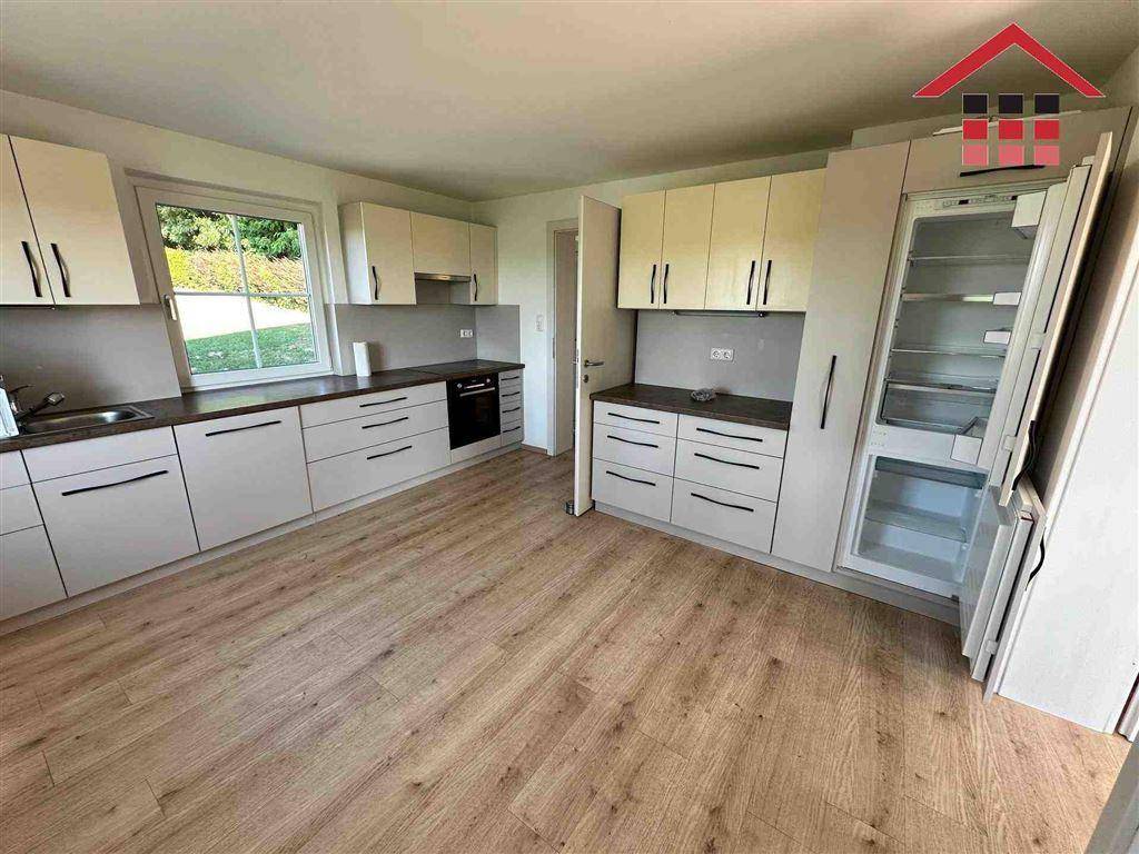 Moderne Einbauküche mit hellen Fronten, Holzboden und Blick ins Grüne.