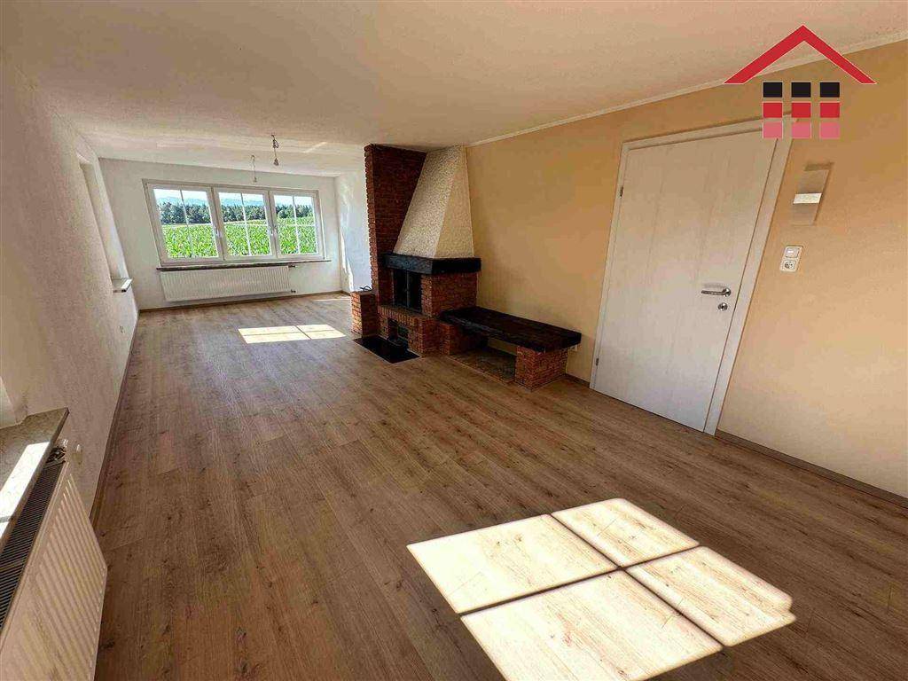 Geräumiges Wohnzimmer mit Kamin, Holzboden und großen Fenstern mit Weitblick.