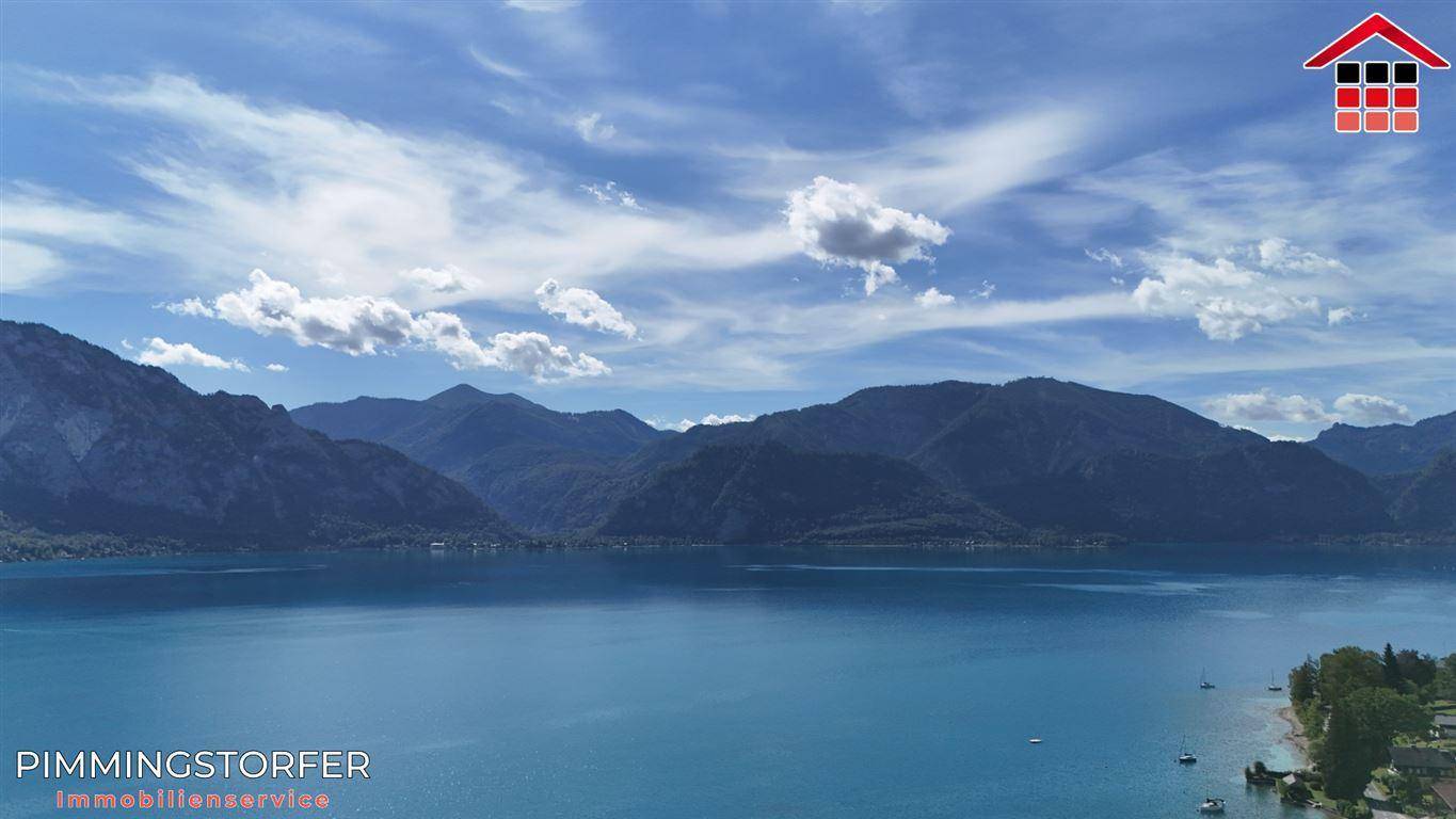Weitläufiger Blick über den ruhigen See und die imposante Berglandschaft unter einem weiten Himmel.