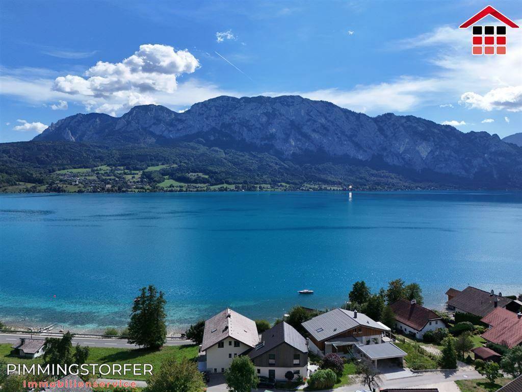 Idyllische Ansicht des Sees mit Uferhäusern und der beeindruckenden Bergkulisse im Hintergrund.