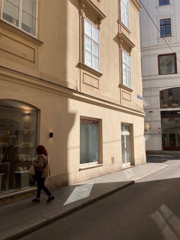 Historisches Eckgebäude mit Schaufenstern und einem Passanten, der im Sonnenlicht vorbeigeht.