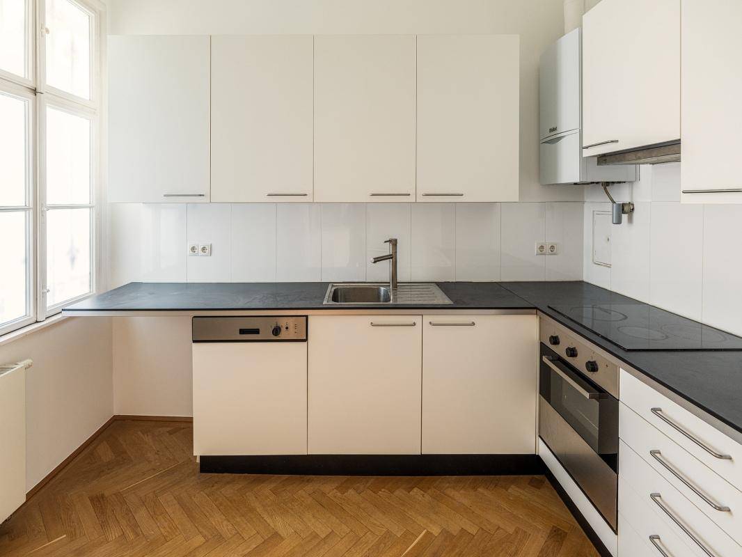 Funktionale Küche mit weißen Schränken, dunkler Arbeitsplatte und integrierten Geräten, inklusive Fenster.
