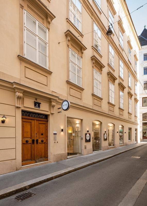 Historische Fassade mit einer großen Holztür und mehreren Geschäftsfronten im Erdgeschoss einer Gasse.
