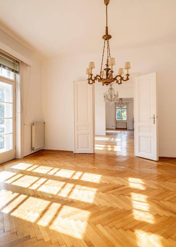 Großzügiges Wohnzimmer mit Fischgrätparkett, hohen Türen und viel natürlichem Licht.